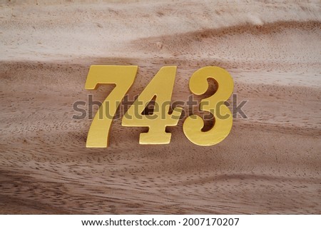 Gold Arabic numerals 743 on a dark brown to off-white wood pattern background.