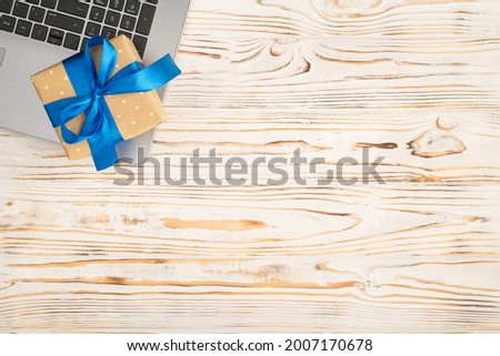 Top view photo of beige gift box with vivid blue ribbon bow on laptop on isolated bright wooden table background with copyspace