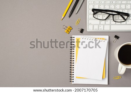 Top view photo of workstation glasses on keyboard cup of coffee stationery binder clips pencil pens and stack of planners on isolated grey background with blank space