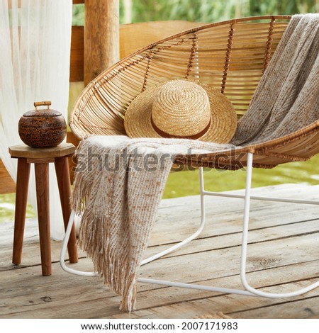 Interior design of summer gazebo by the lake with stylish rattan armchair, coffee table, sofa, pillows, plaid and elegant accessories in modern decor. Summer vibes. Chillout. Template.