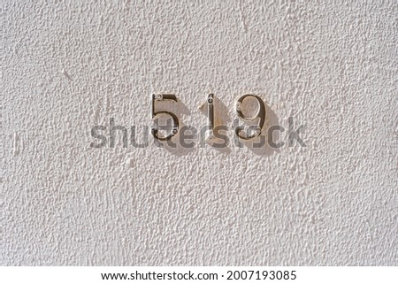 Metal house number 519 on a white stucco wall background, close up