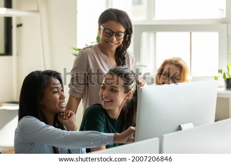 Happy diverse female business team meeting at desktop computer, watching presentation on monitor, talking about work tasks, smiling, laughing. Employee presenting project solution, showing content Royalty-Free Stock Photo #2007206846