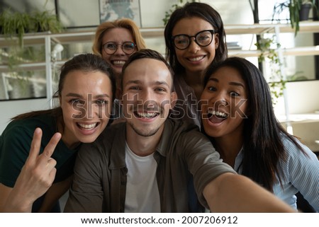 Happy excited diverse business team, mixed race employees of different generations taking office selfie, holding mobile phone, looking at camera, smiling. Head shot portrait, screen view