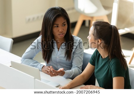 Multiethnic interns girls discussing and completing training task at workplace with laptop. Diverse female students studying foreign language, practicing speaking in school, training center classroom Royalty-Free Stock Photo #2007206945