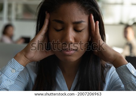 Stressed tired mixed race black office employee suffering from headache, chronic migraine at workplace, feeling strong pain, holding head with closed eyes, getting angry, nervous. Close up head shot Royalty-Free Stock Photo #2007206963
