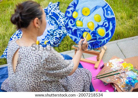 Asian young woman painting picture of lemons on blue blanket in home terrace. High quality photo