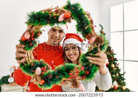 Young couple smiling happy wearing christmas hat at home.