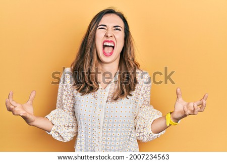 Young hispanic girl wearing casual clothes crazy and mad shouting and yelling with aggressive expression and arms raised. frustration concept. 