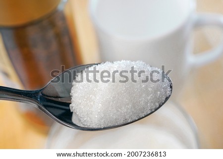 Closeup of spoon of sugar. Spoon of granulated sugar against the background of the white cup and coffee jar. Unhealthy eating concept. Royalty-Free Stock Photo #2007236813
