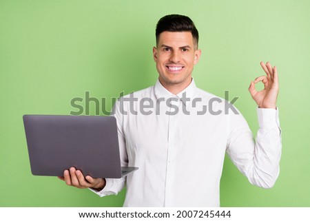 Photo of attractive sweet gentleman wear white shirt smiling showing okey holding modern gadget isolated green color background