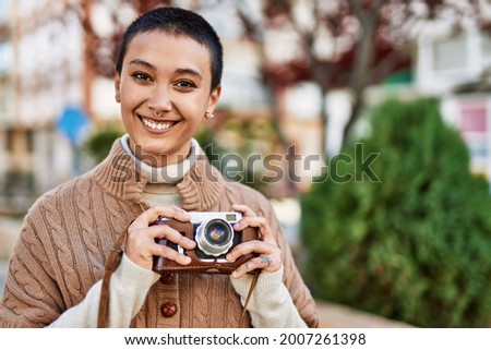 Beautiful hispanic woman with short hair smiling happy outdoors holding vintage camera