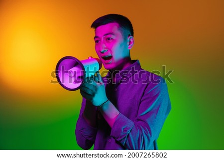 Shout, scream. Portrait of Asian young man isolated on studio background in gradient green yellow neon light, colour filter. Concept of human emotions, facial expression. Copy space for ad.