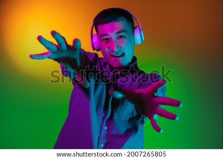 Gesturing. Portrait of Asian young man isolated on studio background in gradient green yellow neon light, colour filter. Concept of human emotions, facial expression. Copy space for ad.