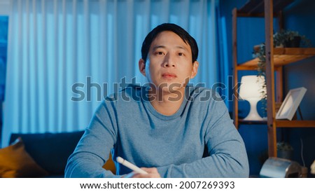Asia businessman looking at camera focus online video call meeting assignment work with colleague on tablet in living room at home overtime at night, Work from home coronavirus pandemic concept. Royalty-Free Stock Photo #2007269393
