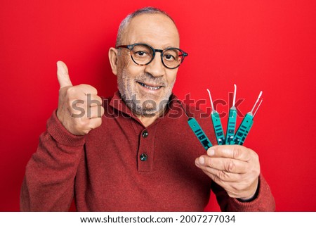 Handsome mature man holding picklock to unlock security door smiling happy and positive, thumb up doing excellent and approval sign 