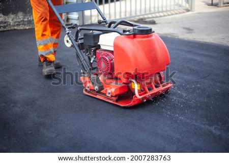 Asphalt laying. Leveling the road. A worker compresses warm asphalt. Road surface repair. Royalty-Free Stock Photo #2007283763