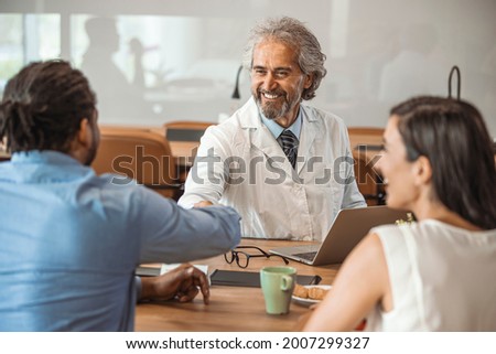 Senior healthcare worker discussing with couple. A photo of happy male doctor shaking hands with patient. Mature medical professional. They are sitting in hospital. Consultation In Doctors Office