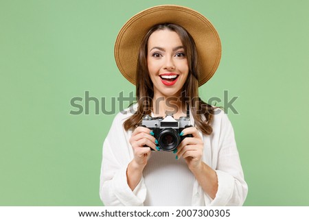 Traveler excited tourist woman in casual clothes hat taking picture on retro vintage photo camera isolated on green background Passenger travel abroad on weekends getaway Air flight journey concept Royalty-Free Stock Photo #2007300305