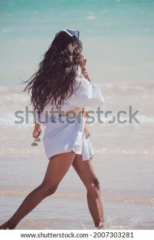 Back view black indian woman walking on the seashore wearing summer clothes enjoying a sunny summer day. Summer Vibes Concept 2021. 