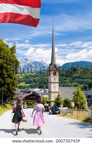 Bischofshofen with couple of women in traditional costumes against main church in Tyrolian Alps, Austria