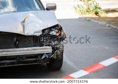 Car accident fenced with red warning tape. Broken hood of car on road. Broken Bumper and Car Headlights with Light On road surface asphalt with copy space. nobody.