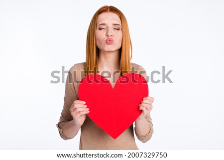 Photo of flirty sweet ginger lady wear beige shirt sending kiss holding big paper heart isolated white color background