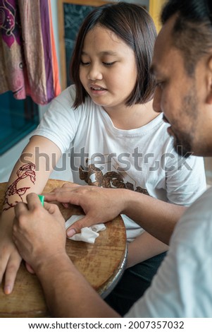 Painting henna ornaments on daughter's hand.
