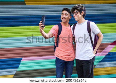 Two gay Latino men taking a selfie on the streets of Mexico City, one dark-skinned and the other light-skinned, hugging