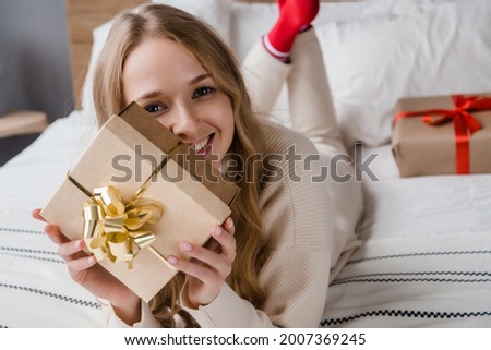 Cute smiling woman with gift box lying in bed and looking at camera. Christmas or birthday celebration concept