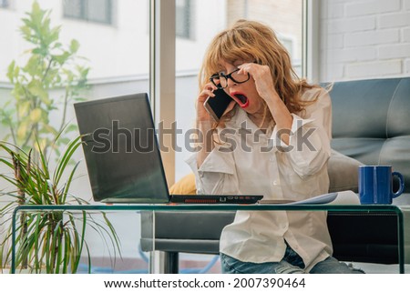woman with mobile phone at home surprised looking at computer