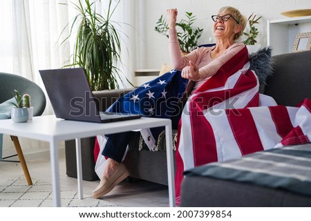 Old American lady watching games, cheering with an American flag suppotting her team.