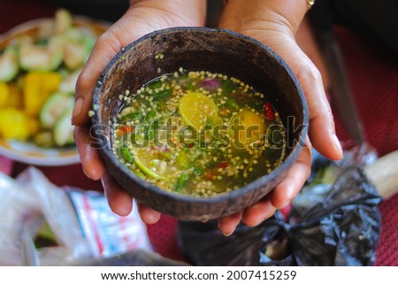 Sambal Jahe or spicy ginger sauce on wood coconut bowl (cobek) with ingredients, green chilies, onions, ginger, MSG, citrus lemon, and salt. Indonesian traditional spicy sauce on hand stock images.