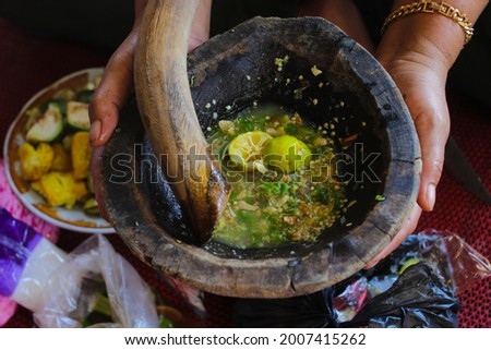 Sambal Jahe or spicy ginger sauce on wood mortar (ulekan kayu) with ingredients, green chilies, onions, ginger, MSG, citrus lemon, and salt. Indonesian traditional spicy sauce on hand stock images.