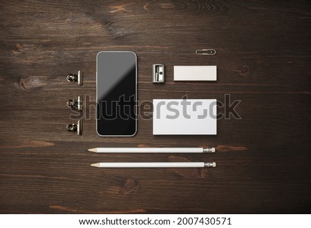 Blank branding mockup. Blank business card, smartphone, pencils, eraser and sharpener on wooden background. Top view. Flat lay.