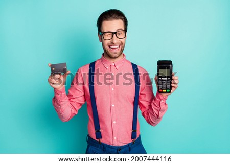 Photo of pretty charming gentleman wear pink shirt glasses holding credit card terminal winking smiling isolated teal color background