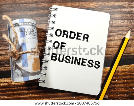 Business concept.Text ORDER OF BUSINESS on notebook with dollar banknote and pencil on a wooden background.