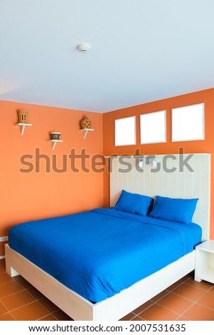 Interior of minimalistic dark blue bedroom with orange walls, cement floor, master bed with photo frame headboard.