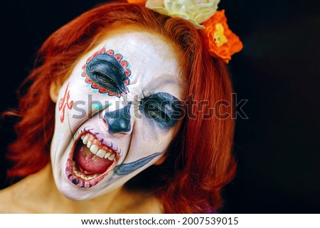 A young woman in day of the dead mask skull face art. Woman with skull makeup and red hair, screaming on dark background close up