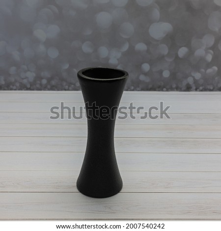 A ceramic black flower vase stands on a wooden table. A graceful hourglass-like silhouette. Gray background
