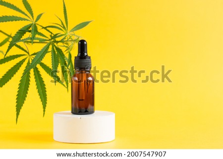 Amber glass cosmetic bottles with CBD oil and hemp leaves stand on the podium. Cosmetics CBD oil on a yellow background. Copy space for text. Royalty-Free Stock Photo #2007547907