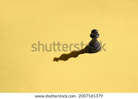 Black pawn with kings shadow on yellow background Royalty-Free Stock Photo #2007565379