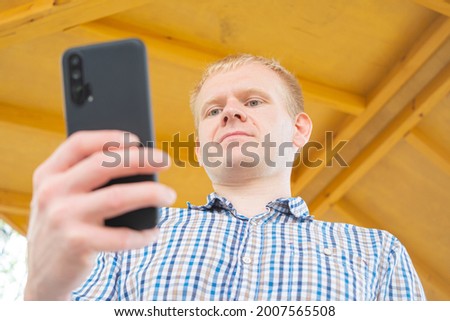 Young blond man in a plaid shirt with a mobile phone in his hands. The concept of communication, freelancing, cellular communication, walking.