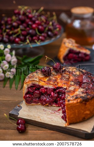 Tall cherry pie stuffed with cherry berries with intertwined ferkh lying on a board on a wooden background 
