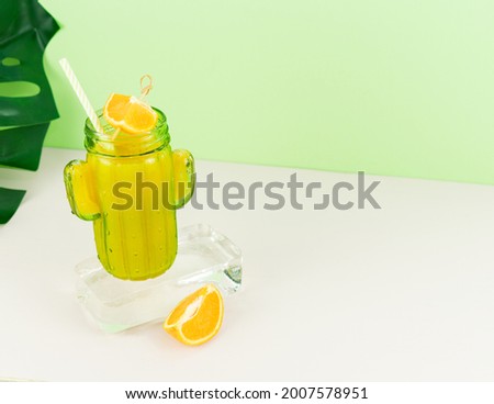 Orange juice in cactus shaped glass on ice block with fruit decoration. Copy space.