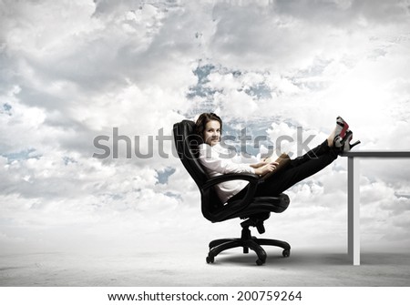 Young businesswoman sitting in chair with legs on table and reading book