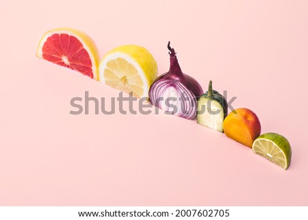 Conceptual creative still life with fruits and vegetables: cucumber, onion, lemon, lime, grapefruit, apricot. Multicolored conceptual composition on pink background