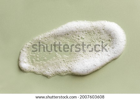 Face cleansing mousse sample. White cleanser foam bubbles on green background. Soap, shower gel, shampoo foam texture closeup. Royalty-Free Stock Photo #2007603608