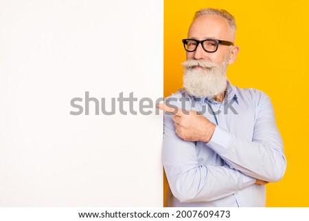 Photo of cheerful old man point finger empty space white banner smile isolated on yellow color background