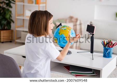 Profile side photo of young excited little girl distance education look cellphone tripod sit desk learn lesson indoors