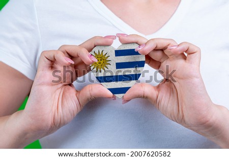 Woman in white t-shirt holds a heart in the form flag Uruguay on her chest. Photo for a postcard on Flag Day, Independence Day, travel, patriotism, other holiday